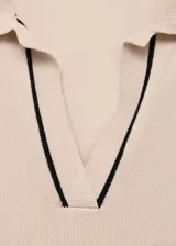 Jersey de punto fino color beige con cuello polo y solapa, manga larga con puños acanalados y ribetes en contraste.