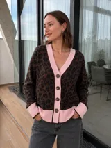 Saco tipo cardigan de tejido bremer con estampado animal print en tonos marrones y negros. Presenta cuello en V, cierre frontal con botones y detalles en color rosa en los bordes, puños y ruedo.