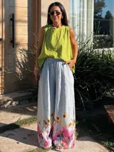 Pantalón ancho de tiro alto, color naranja vibrante, con estampado floral grande en tonos rosados y marrones en la parte inferior.