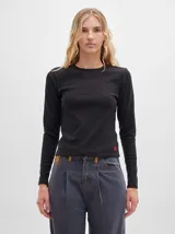 Camiseta negra de manga larga, con tejido acanalado, cuello redondo a la base y corte tipo crop. Presenta costuras rojas a la vista y un logo "M" bordado en rojo en el lateral izquierdo.