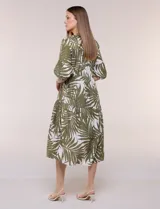 Vestido midi de silueta holgada en color blanco con estampado de hojas verdes. Presenta escote en V con cuello mao y botones frontales en la pechera, mangas tres cuartos abullonadas con puños elásticos y falda de corte evasé con niveles fruncidos.