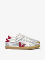 Championes Veja modelo Volley, de color plateado metalizado con detalles en rojo en el logo lateral y el talón. Presenta suela de goma color caramelo y cordones blancos.
