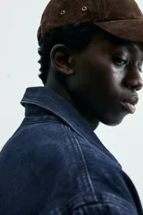 Chaqueta de denim de algodón en color azul oscuro con corte relaxed fit. Presenta cuello de solapa, cierre frontal con botones metálicos y tres bolsillos de parche en el delantero. Las mangas son largas con puños abotonados.