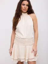Vestido corto color beige con diseño a rayas sutiles, cuello halter y espalda descubierta. Cuenta con una faja fruncida en la cintura y falda con volados en el borde inferior.