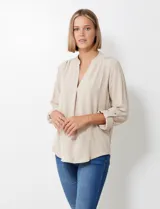 Blusa de gasa color beige, marca Floral & Ivy, con cuello a la base y escote en V. Las mangas son largas y regulables con presilla y botón.