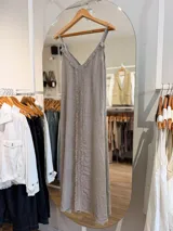 Vestido largo de lino color beige, con escote en V, tiras finas regulables y detalles de flecos en la parte frontal.