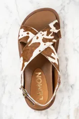 Sandalias con tiras cruzadas de cuero con estampado animal print de vaca en tonos marrón y blanco. Tira trasera con hebilla ajustable. Suela plana color marrón.