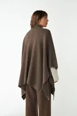 Capa color crudo de tejido de punto 100% lana fina, con cuello alto, cierre frontal con botones, bolsillos delanteros y corte asimétrico.