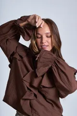 Blusa de color marrón con escote en V, mangas largas abullonadas con puños elásticos y detalles de volados en los hombros y el frente.
