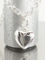 Collar con cadena de eslabones gruesos plateados y un dije colgante de corazón liso y pulido.