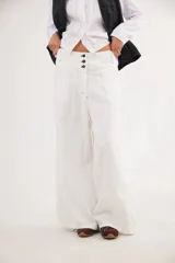 Pantalón de jean con diseño de tiro medio-bajo y piernas anchas. Presenta una pretina ancha con cierre de tres botones metálicos frontales, pinzas decorativas en la cintura y bolsillos delanteros funcionales.