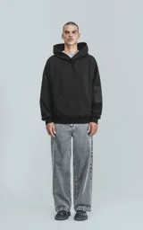 Hoodie oversize de algodón, color negro, con capucha forrada, bolsillo frontal tipo canguro y bolsillo con cierre en la manga estilo bomber.