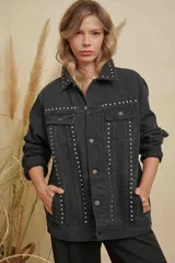 Campera de jean color negro con diseño de tachas metálicas plateadas distribuidas en el cuello, los bolsillos frontales y a lo largo de la parte delantera. Cuenta con cierre frontal de botones metálicos y mangas largas.