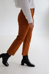 Pantalón cropped de tiro medio con acabado engomado, corte recto y bolsillos laterales. Presenta cierre frontal con botón y costuras a tono.