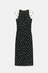 Vestido midi de lunares, color negro con lunares blancos, escote en V y mangas sisa con hombreras. Presenta frunces laterales en la cintura y cierre en la espalda con cremallera oculta.