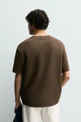 Camiseta relaxed fit color marrón, confeccionada en tejido con estructura, cuello redondo y manga corta.