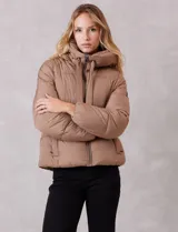 Campera puffer de corte recto y acabado mate, con diseño de bloques horizontales acolchados. Presenta capucha integrada con cordones de ajuste, cierre frontal metálico y bolsillos laterales invisibles. Incluye puños elásticos internos para mayor protección contra el frío.