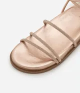 Sandalia plana color dorado con acabado metalizado, diseño de tiras finas, algunas de ellas con incrustaciones de brillo, y cierre ajustable con hebilla al tobillo.