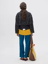 Campera de denim color negro con diseño de flecos en la parte frontal, cuello camisero y cierre frontal con botones metálicos.