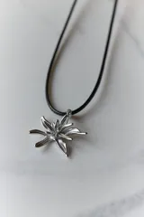 Collar con dije de acero quirúrgico en forma de flor de lirio, montado sobre un tiento de cuero encerado largo.