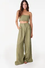 Pantalón de lino blanco de corte ancho y fluido, con cintura alta que incorpora una sobrepretina ancha desmontable con pliegues horizontales.