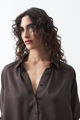 Camisa negra de corte relajado y caída fluida, con cuello clásico, escote en V y cierre frontal con botones forrados. Presenta mangas largas con puños abotonados.