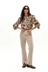 Pantalón de gamuza color arena, de corte recto con tajos en el ruedo. Tiene cintura de tiro medio con elástico interno y cierre frontal con gancho metálico escondido.