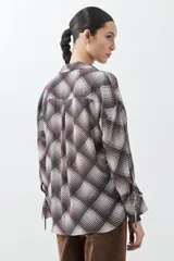 Camisa de manga larga con estampado escocés en tonos chocolate, blanco y gris. Presenta cuello camisero, cierre frontal con lazos y puños con lazos ajustables.