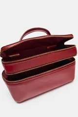 Bolso tipo vanity color tostado con pespuntes en contraste. Cuenta con asa de mano superior, doble compartimento con cierre de cremallera y correa bandolera ajustable y extraíble.