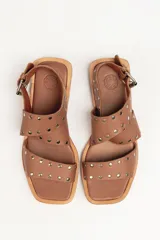 Sandalias bajas de cuero negro con tachas plateadas, tiras cruzadas y hebilla al tobillo.