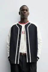Chaqueta de corte relajado con diseño color block, cuerpo en color azul marino y mangas en color blanco. Presenta cuello redondo, cierre frontal con botones y puños de rib a rayas.