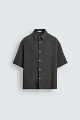 Camisa de corte relajado con textura de rayas verticales, cuello solapa y manga corta. Presenta cierre frontal con botones a tono.