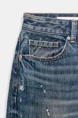 Bermuda tipo jorts de tiro medio confeccionada en denim azul con efecto lavado. Presenta diseño de cinco bolsillos, roturas decorativas y ruedo desflecado.