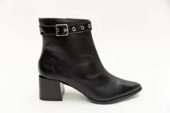 Botas de cuero negro, de caña baja, punta fina y taco cuadrado. Presentan un aplique charolado al tono, una correa con hebilla y ojales metálicos.