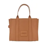 Cartera tipo tote de cuero granulado en color gris, con diseño estructurado y asas superiores. Presenta el logo estampado en el frente con la inscripción The Tote Bag Marc Jacobs.