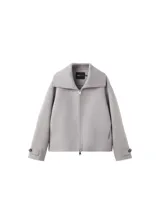 Chaqueta gris de diseño corto y holgado, con cuello alto envolvente, mangas anchas y puños ajustables con tiras y botones. Cuenta con bolsillos laterales y cierre frontal oculto.