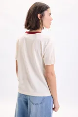Remera manga corta de color crudo, con cuello redondo en tono bordó y estampa frontal con texto en el pecho.