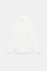 Camisa amplia blanca de cuello alto y manga larga, con cierre frontal de botones.