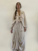 Pollera midi de corte asimétrico y holgado, inspirada en la forma de pantalón babucha. Confeccionada en tela crepé color beige, presenta cintura elástica, bolsillos laterales amplios y un detalle de etiqueta con texto en el bolsillo derecho.