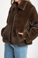 Abrigo de piel sintética en color marrón, con cuello clásico, cierre frontal con cremallera y mangas largas.