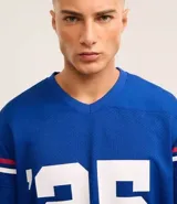 Remera deportiva azul con tecnología Dry, cuello en V, manga corta con estampado lettering y rayas contrastantes, estampado lettering NFL Giants.
