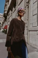 Abrigo de piel color marrón, con cuello redondo, manga larga, cierre frontal con botones y dos bolsillos delanteros de plastrón.