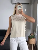 Blusa blanca sin mangas, de símil lino, con cuello alto y detalle de encaje calado y volados en el escote.