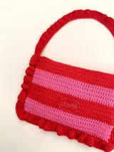 Cartera tipo shoulder bag tejida a crochet en hilo de algodón, con diseño a rayas en tonos de rojo y rosado, y detalles de volados en los bordes y la manija de hombro.