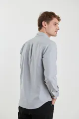 Camisa de vestir blanca de manga larga, con cuello abotonado, bolsillo frontal y botones en tono madera.
