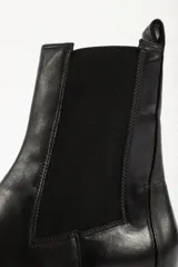 Bota tipo Chelsea de cuero negro con paneles elásticos laterales y suela track dentada de goma.