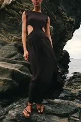 Vestido midi de color negro, sin mangas, con cuello redondo y aberturas laterales en la cintura (cut out). La parte superior es de punto liso y la falda presenta una textura plisada y ligera.