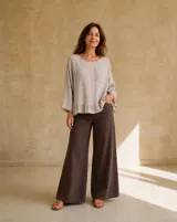 Blusa de lino color beige, de manga larga amplia, cuello redondo y detalle de bolsillo aplicado en el pecho con aplique bordado. Presenta un delicado volado fruncido en el borde inferior.
