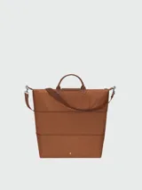 Bolso de viaje Longchamp modelo Le Pliage Original, de diseño ampliable, confeccionado en nylon negro con detalles en cuero marrón en las asas y solapa frontal con cierre de botón a presión. Incluye correa ajustable y extraíble.