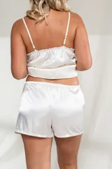Conjunto de satén color blanco, compuesto por un top con breteles finos y detalles de puntilla en el escote, y un short con cintura elástica.